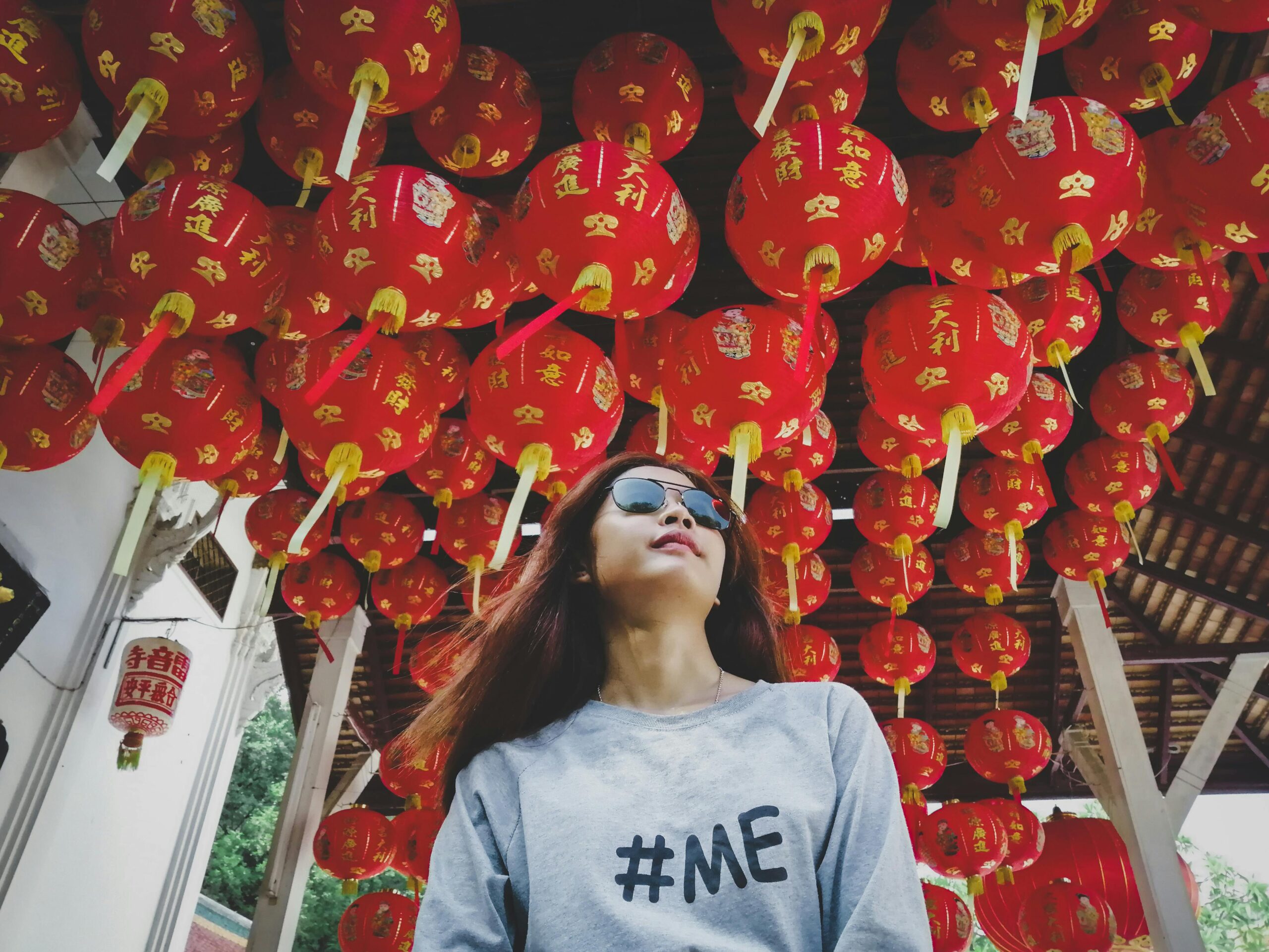 Low angle shot of a woman with sunglasses surrounded by vibrant red Chinese lanterns.